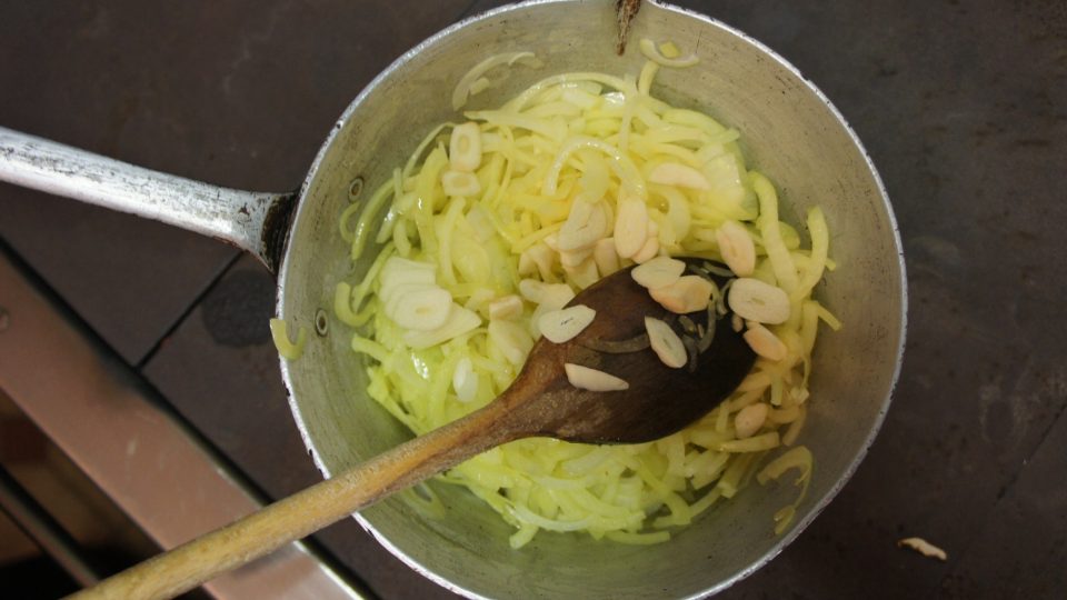 V kastrolu si na husím sádle a oleji zpěníme na silná kolečka nakrájenou cibuli. Přidáme na plátky nakrájený česnek, který polévku provoní